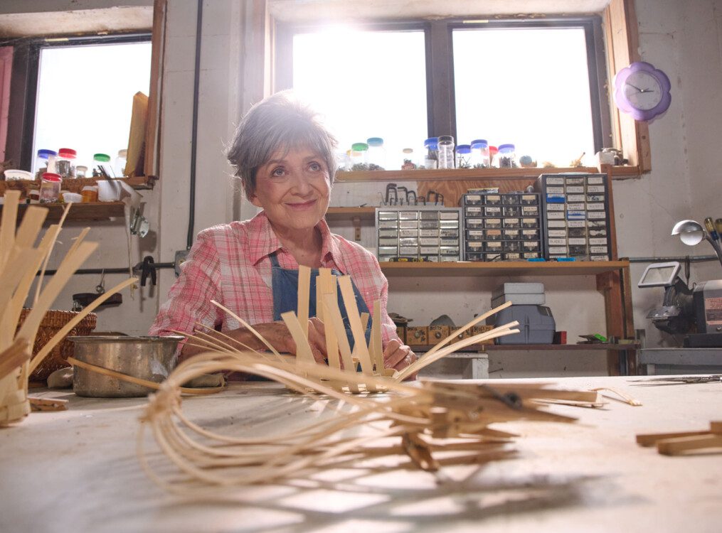 senior woman smiles and looks at an off-camera instructor during a basket-weaving class
