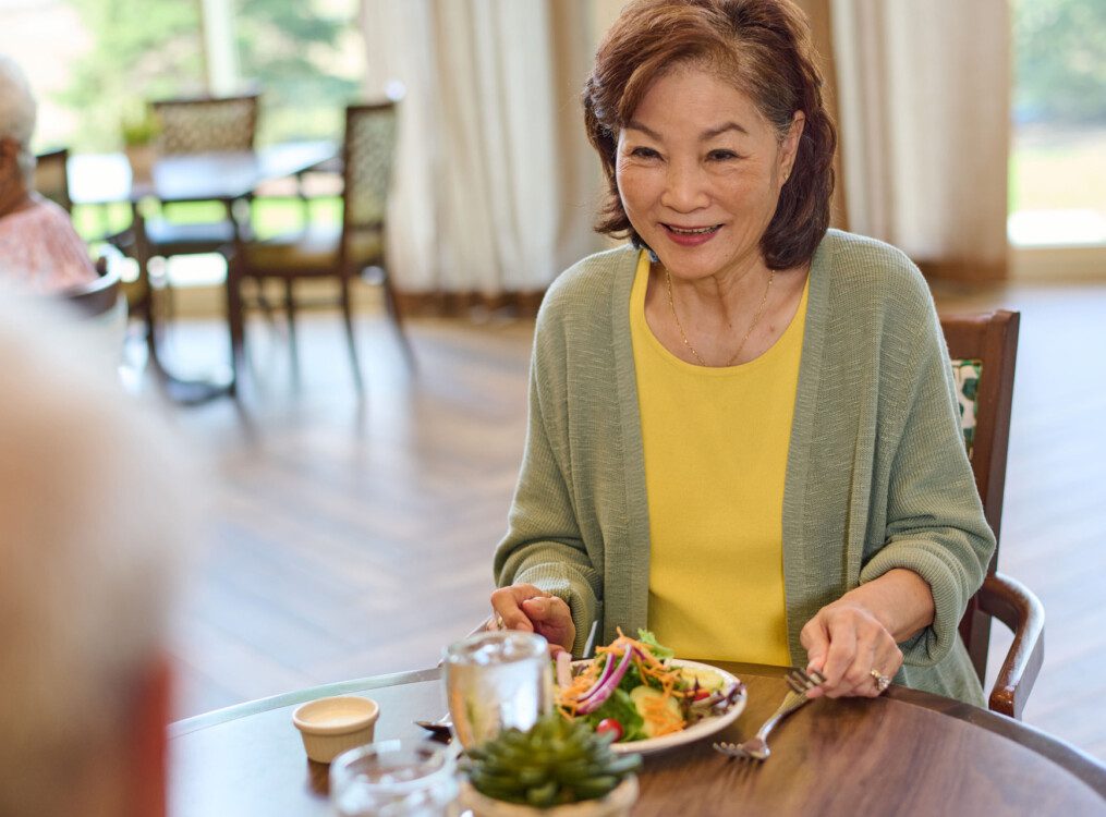 senior woman smiles at her companion while enjoying a healthy lunch in their senior dining room