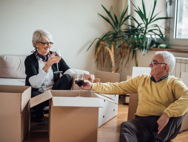 Senior couple clinking wine glasses as they unpack boxes.