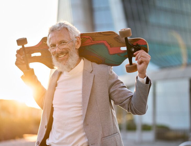 Happy cool older senior business man skater holding skateboard in city.