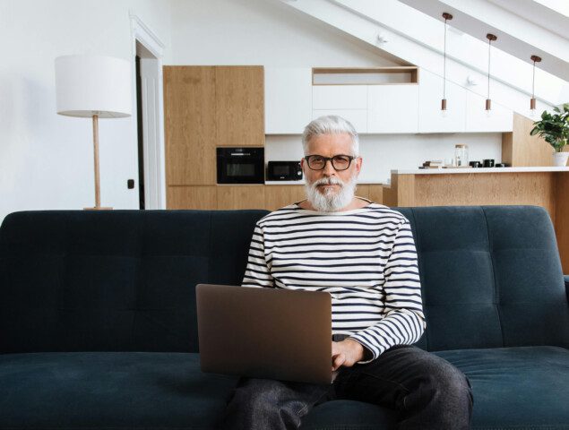 Man with laptop on couch in modern living room with kitchen background.